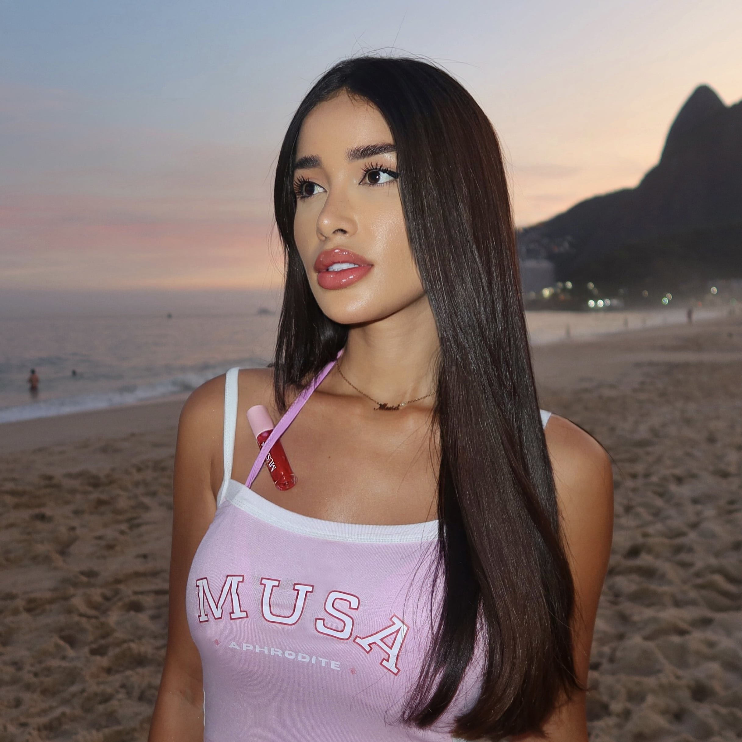 An aesthetic girl wearing a pink crop top inspired by Brazilian t-shirts. She has a red glitter lip oil attached to her bikini.